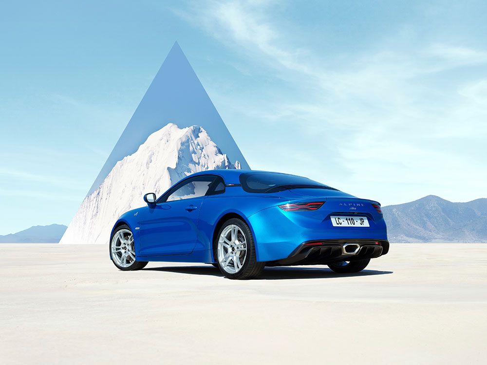 Zu sehen ist ein blauer Alpine A110 GT mit silbernen Felgen zu sehen. Dieser wird auf weißen Kies geparkt und man sieht eine Bergansicht im Hintergrund.